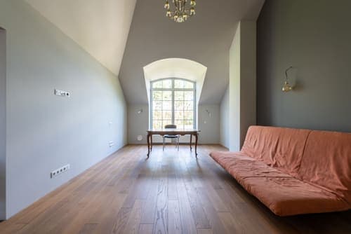 Minimalist room with chandelier, large window, sofa, and wooden floor creates a serene atmosphere.