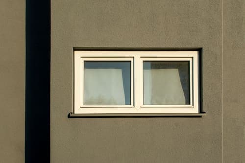 A minimalist white window on a textured concrete wall casting shadows in sunlight.